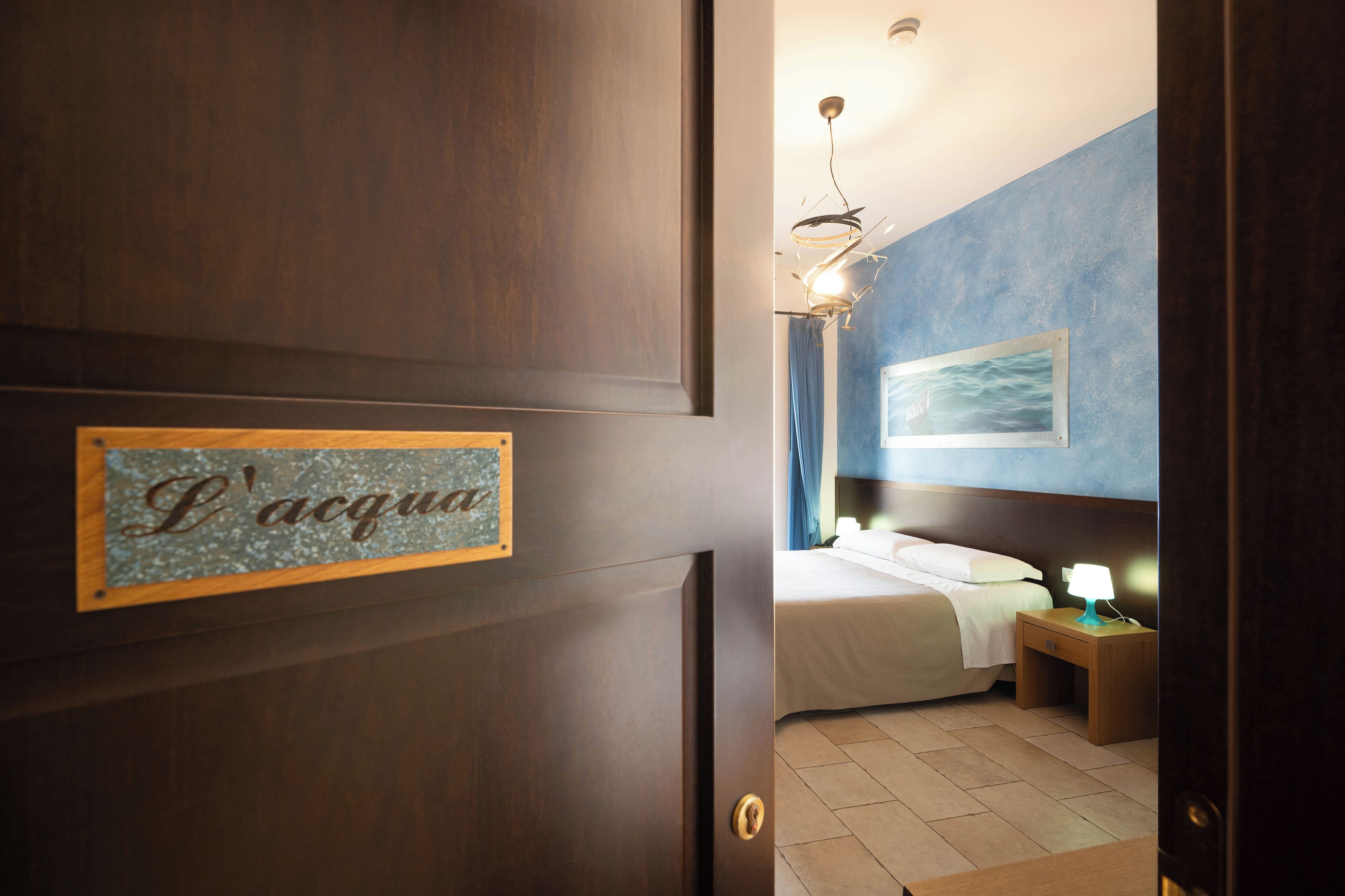 Una camera d'albergo con una porta in legno, un letto con biancheria bianca, un comodino con una lampada e un quadro appeso al muro.