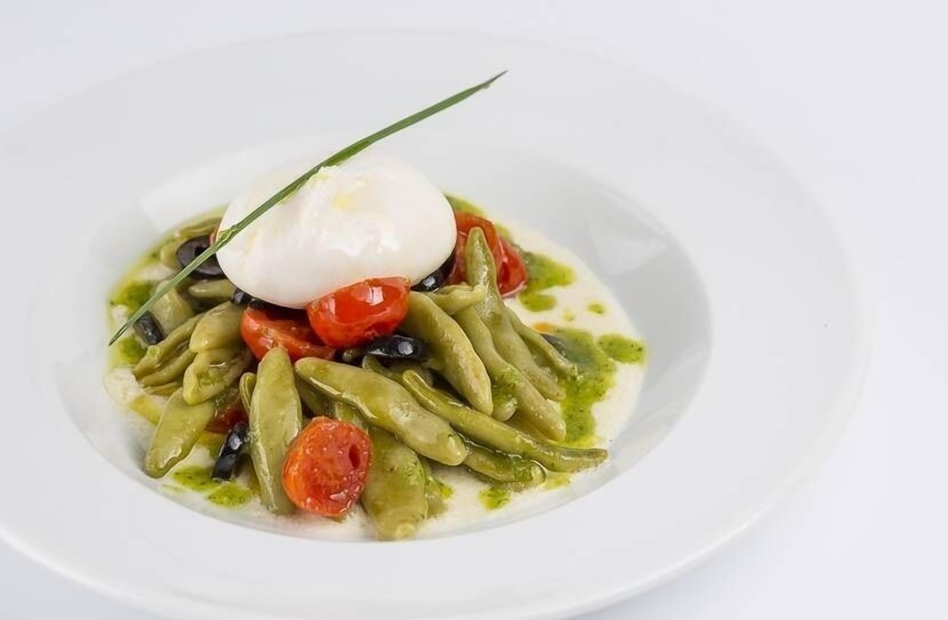 A white plate with a poached egg, green beans, cherry tomatoes, and a drizzle of green sauce.