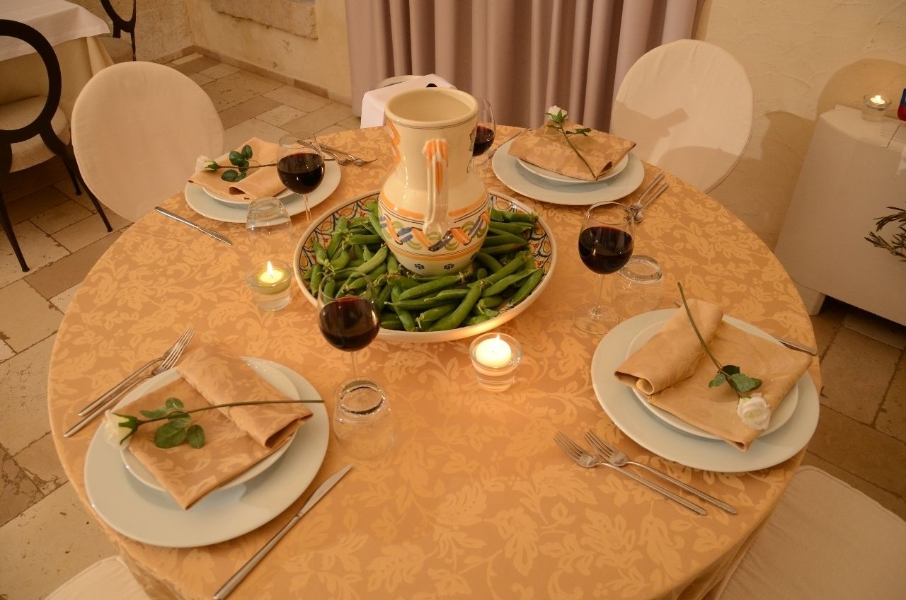 A round dining table set with plates, cutlery, a pitcher, and green beans.