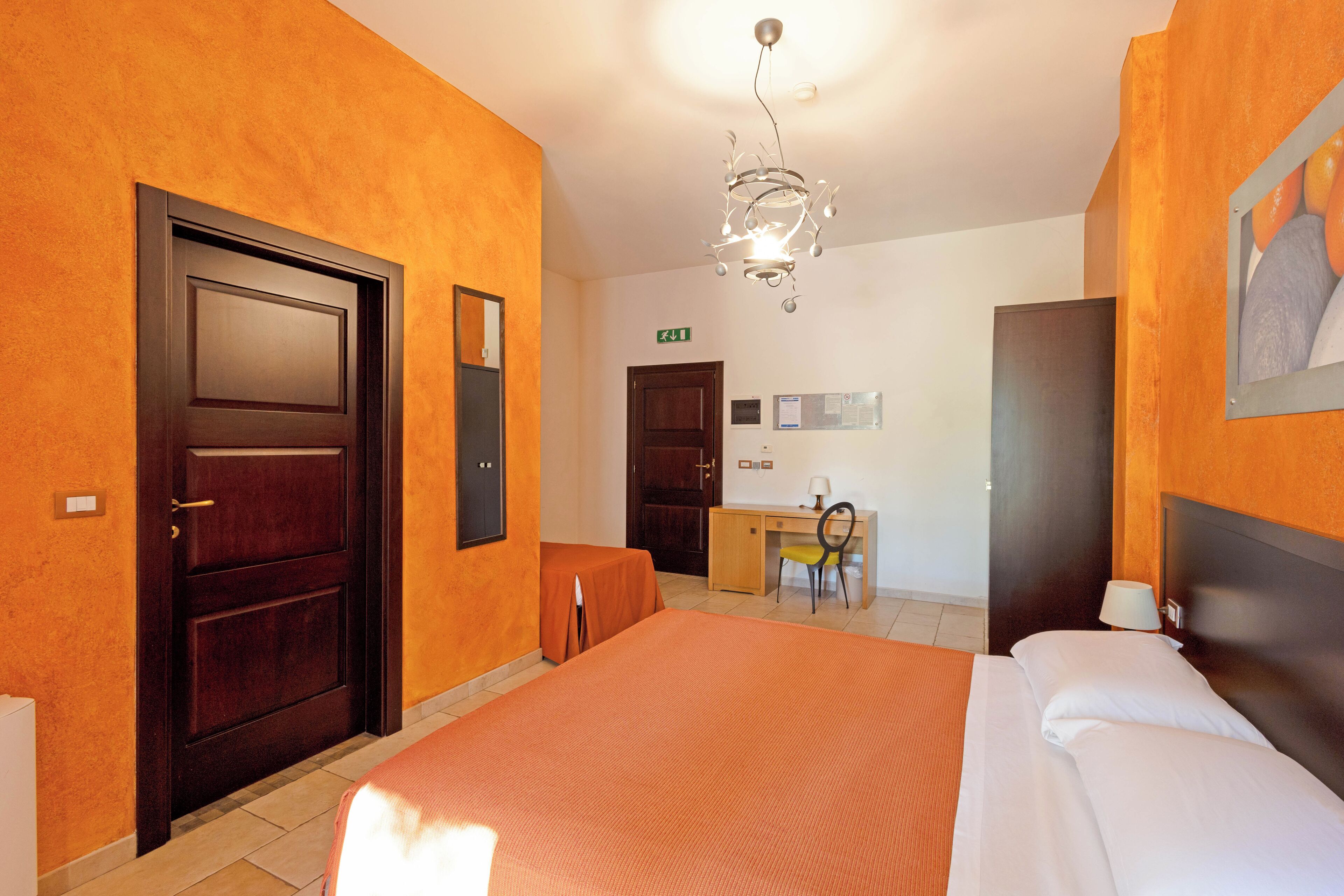 A hotel room with a large bed, a desk, a chair, and a desk lamp.