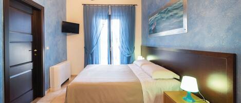 A bedroom with a bed, a nightstand with a lamp, a TV on the wall, and a painting.