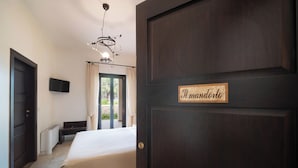 A hotel room with a dark wooden door, a bed, a TV mounted on the wall, and a window with curtains. - Agriturismo Tenuta Chianchizza (Monopoli)