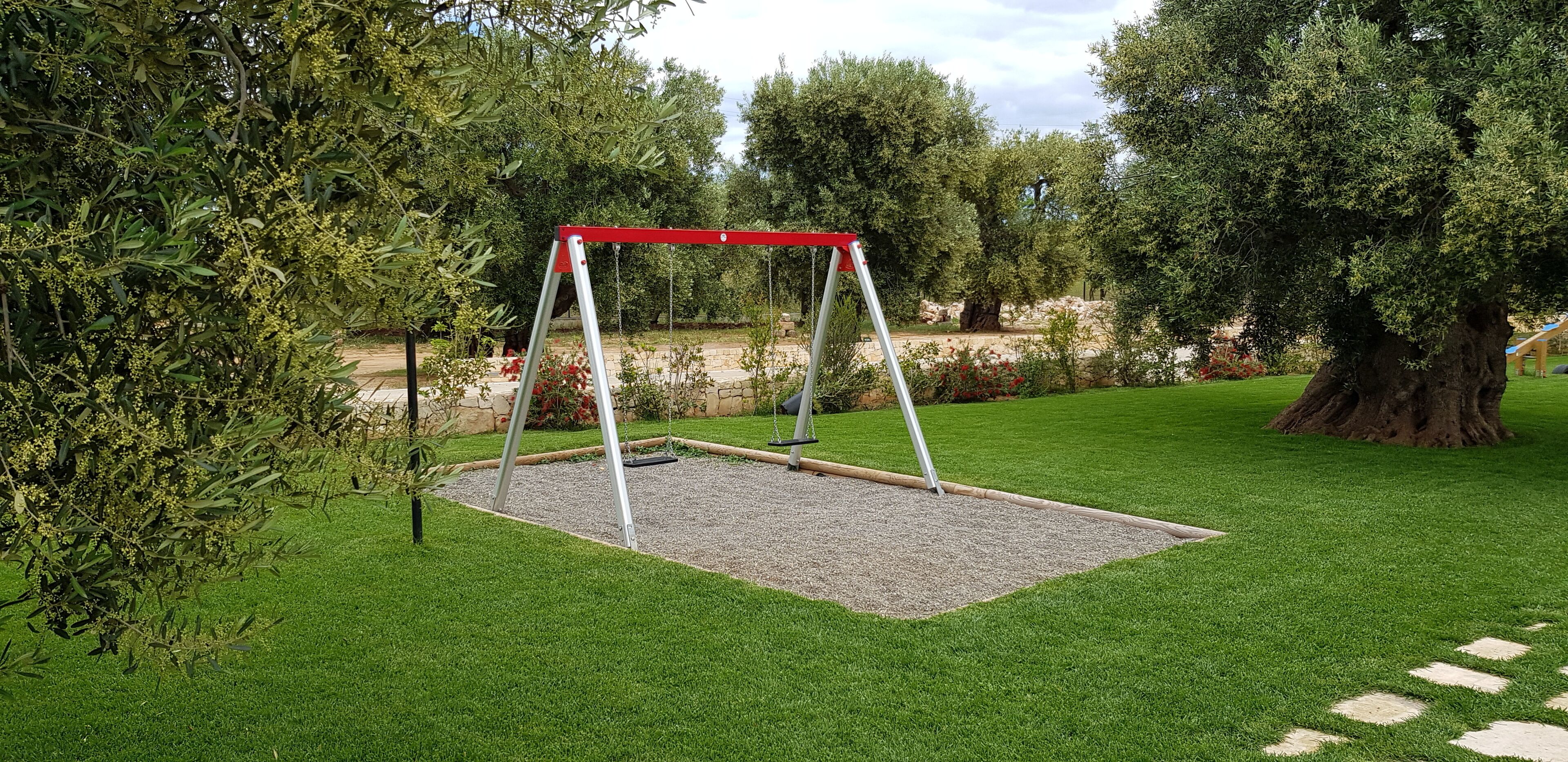 A swing set in a grassy area with trees and a stone wall in the background.