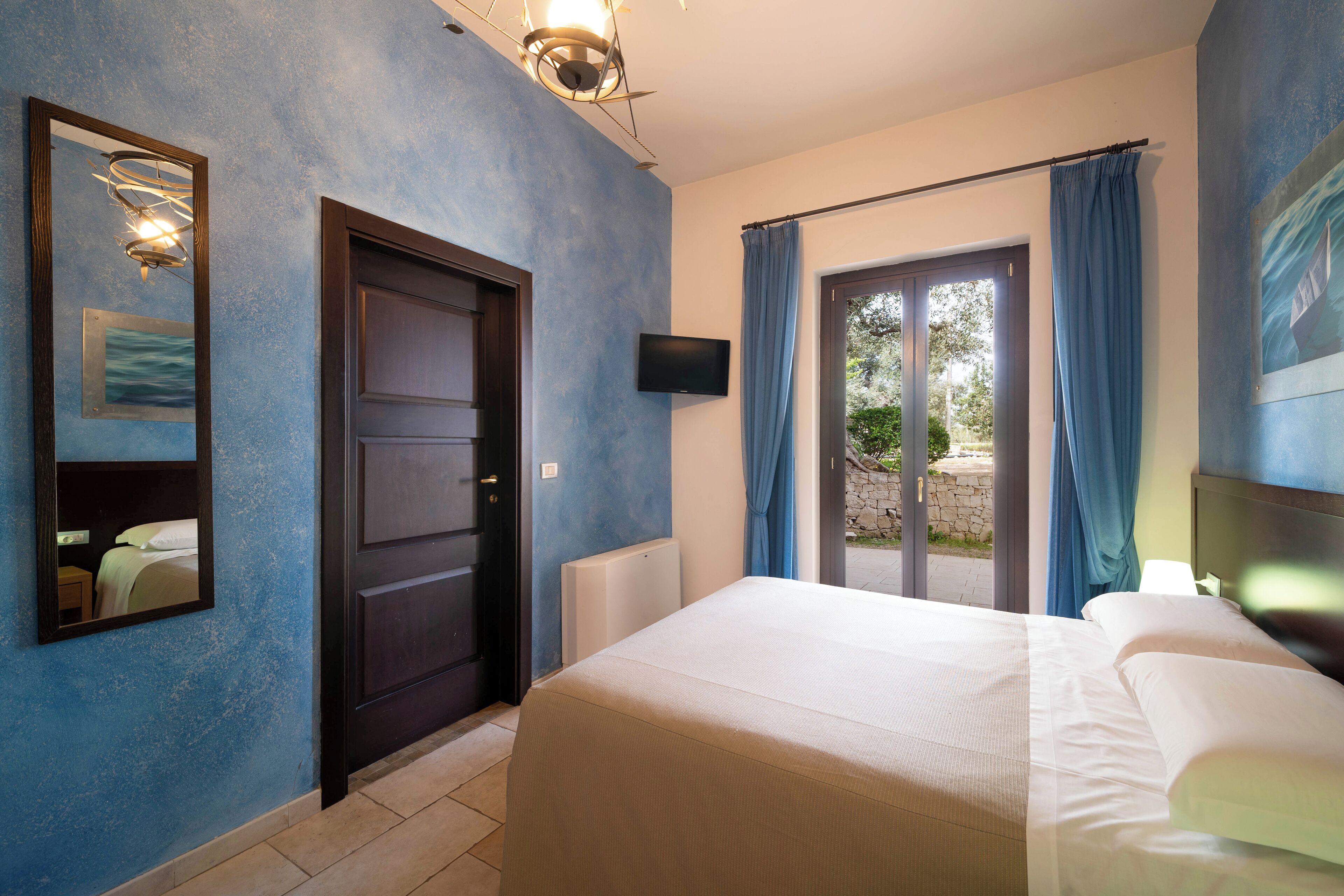 Een hotelkamer met een bed, een deur, een televisie en uitzicht door de glazen deur.