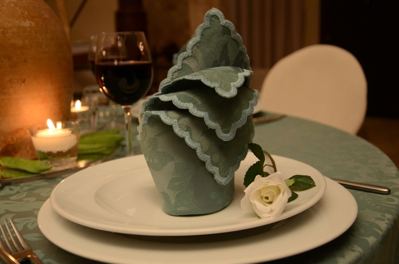 Une table dressée avec un pichet en céramique décoratif, une assiette blanche ornée d’une rose et un verre de vin rouge.