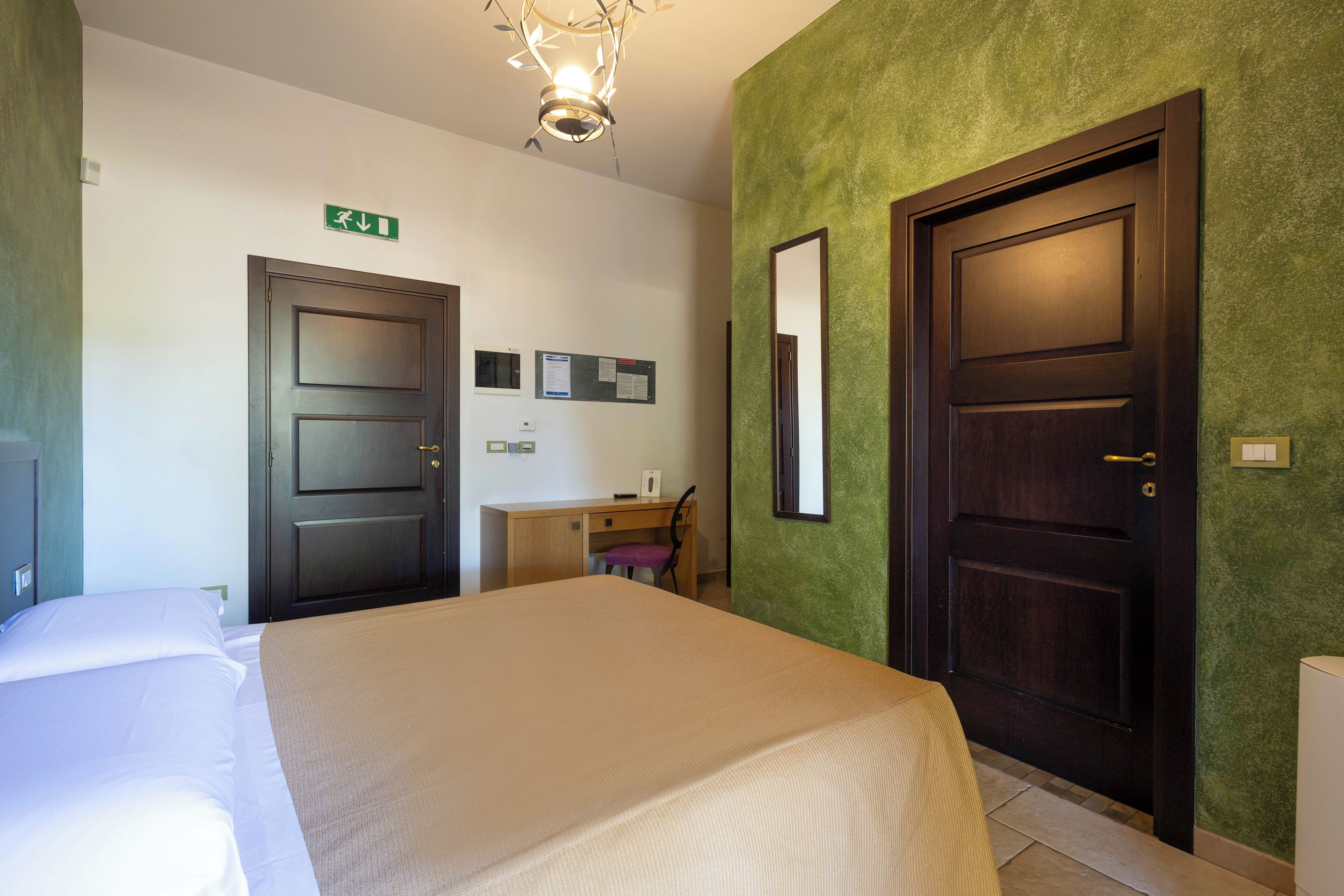 A hotel room with a bed, a desk, a chair, and two doors.