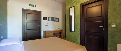 A hotel room with a bed, a desk, a chair, and two doors.