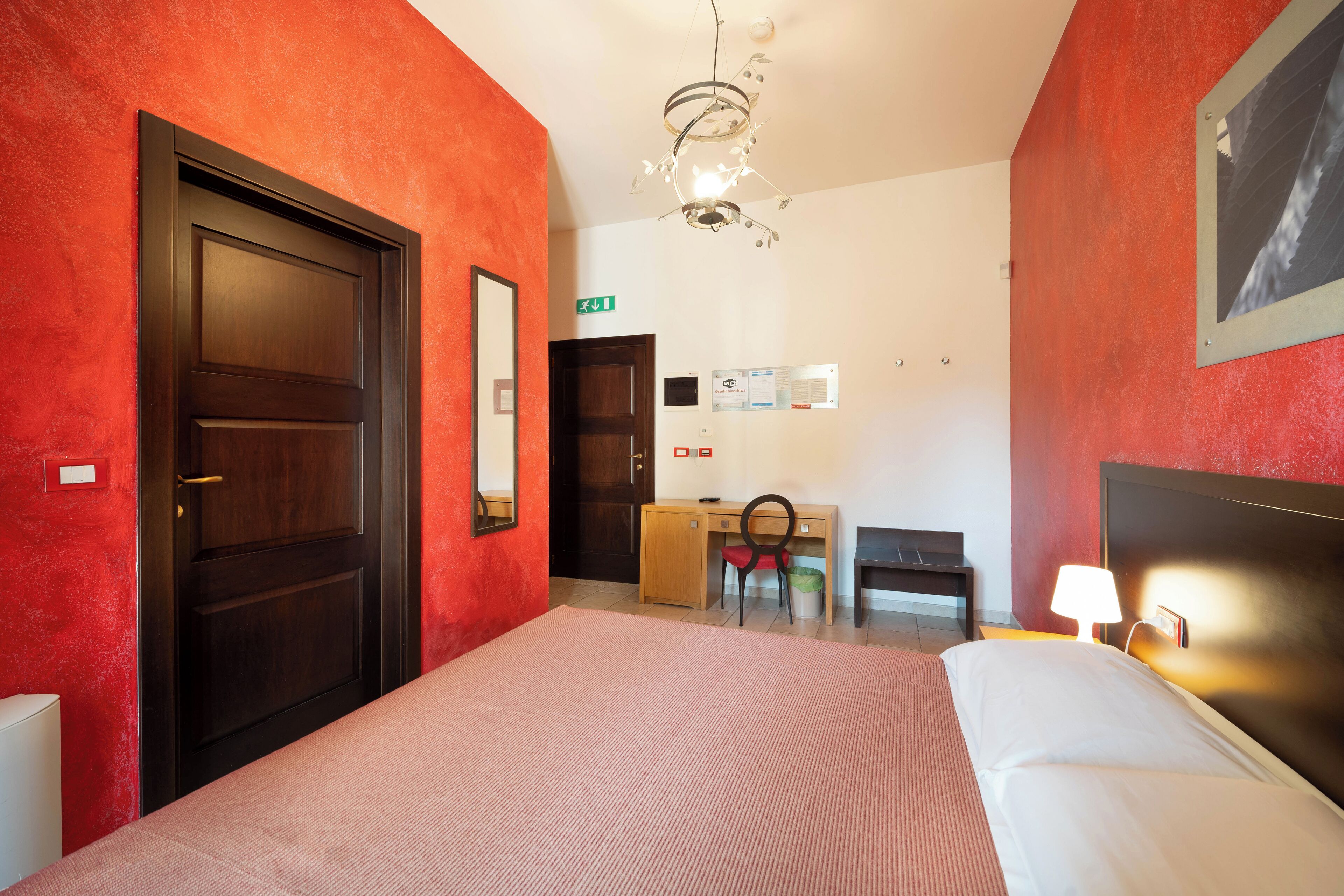 Una habitación de hotel con cama, escritorio, silla y lámpara en el techo.