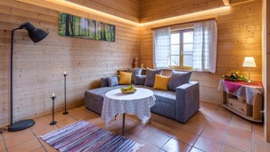 L’intérieur chaleureux d’un chalet, avec un décor en bois, un ensemble de canapés, une table ronde, un lampadaire et un tableau représentant une forêt.