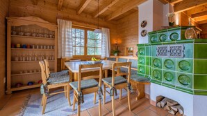 L’intérieur chaleureux d’un chalet avec une table à manger en bois, des chaises, un banc et un coin cuisine carrelé de vert.