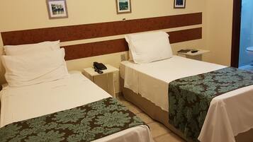 Quarto de hotel com duas camas, mesa de cabeceira com telefone e quadros nas paredes.