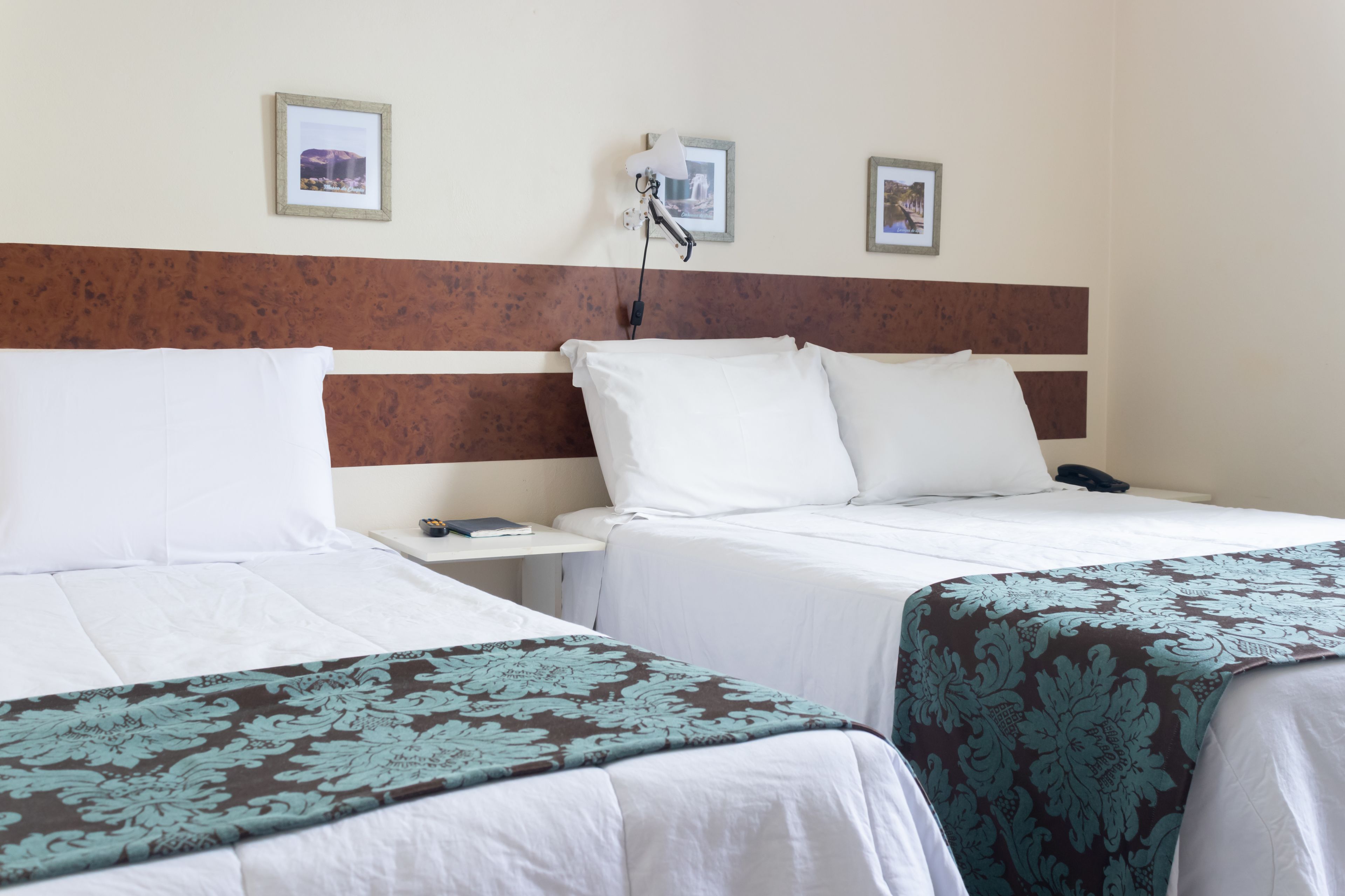 A hotel room with two beds, a nightstand with a phone, and framed pictures on the wall.
