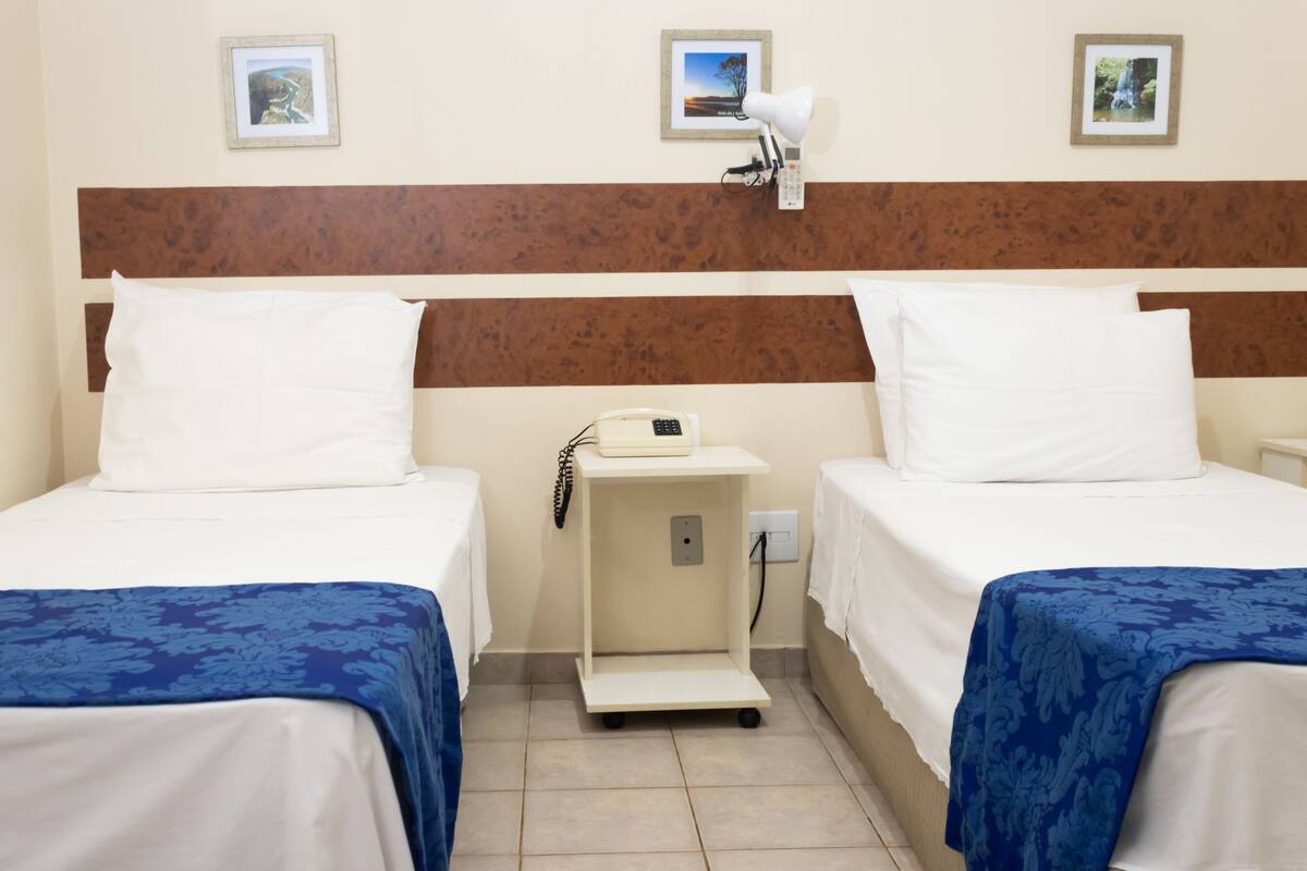 A hotel room with two beds, a nightstand with a lamp, and a small table.