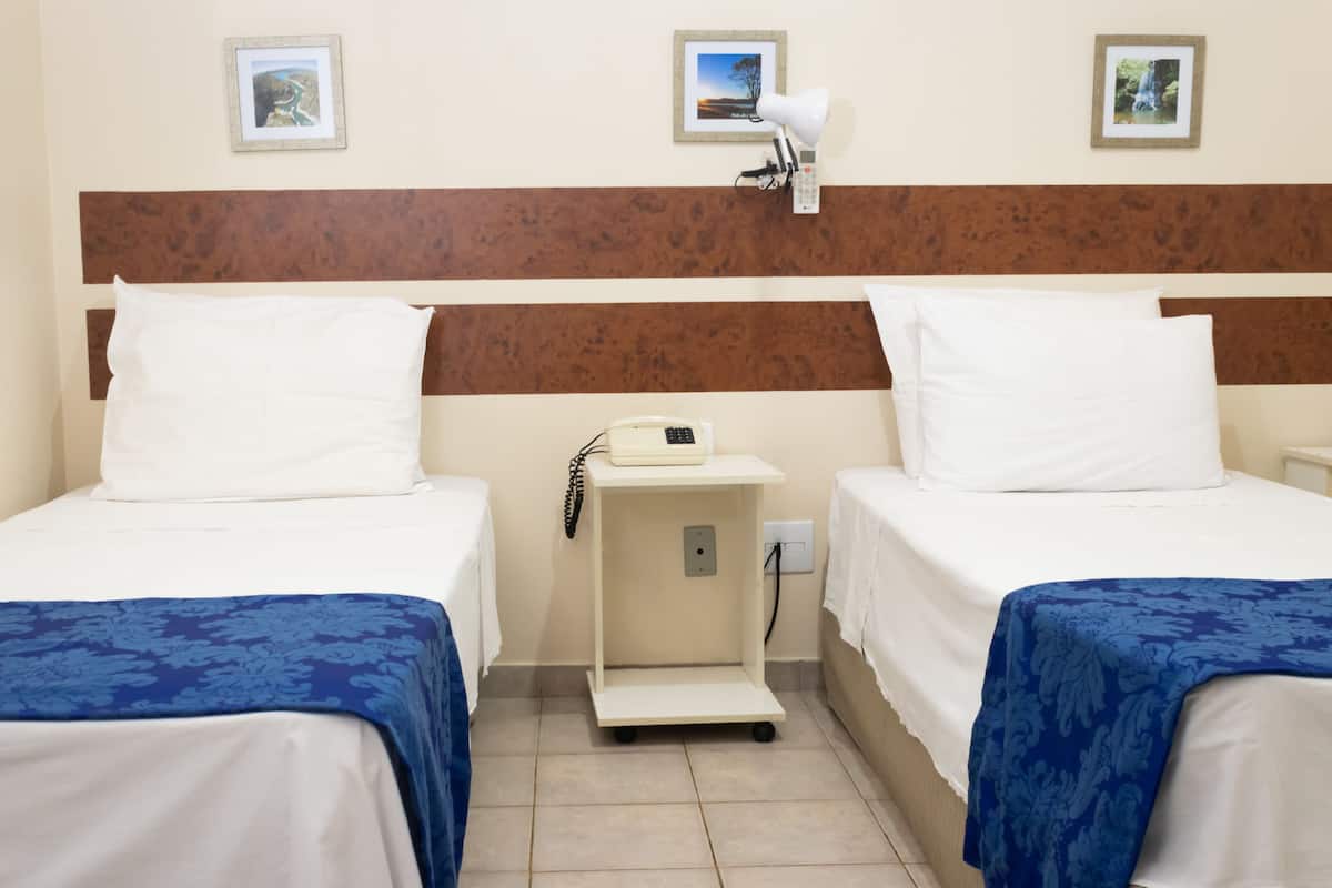 A hotel room with two beds, a nightstand, a lamp, and a small shelf with a phone.