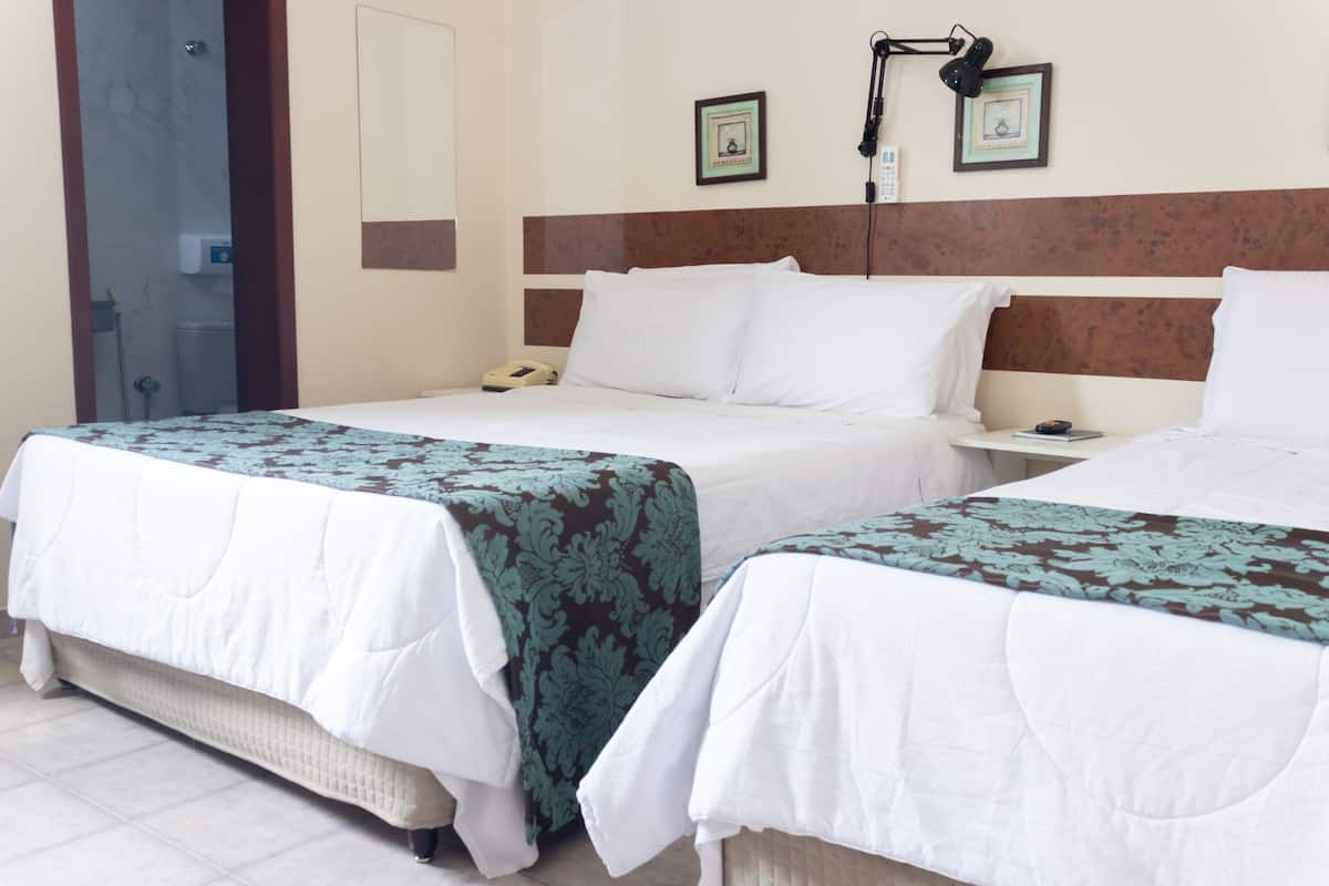 A hotel room with two beds, a bedside table, a lamp, and a framed picture on the wall.
