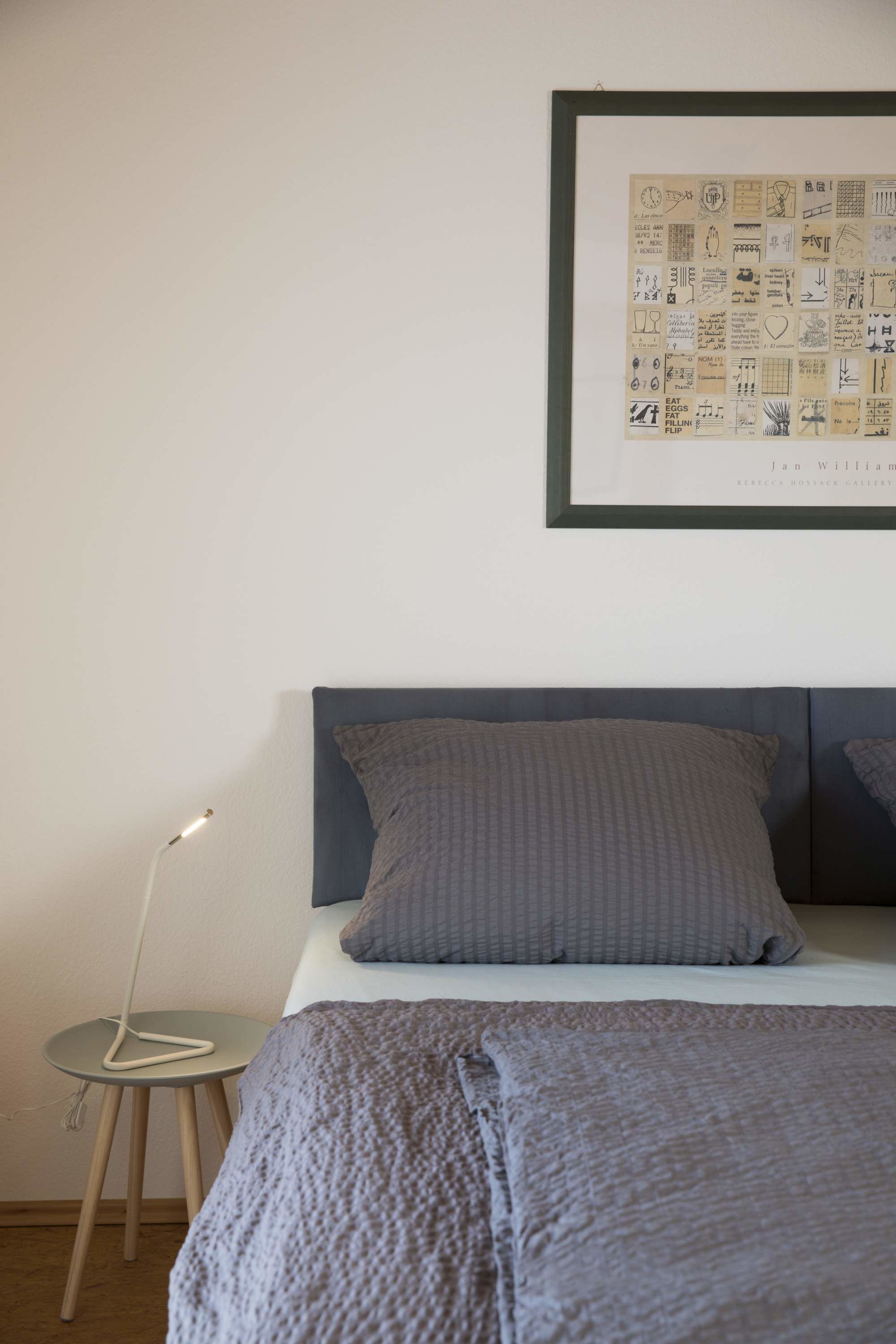 Een slaapkamer met een bed, een lijst met een foto aan de muur en een nachtkastje met een lamp.