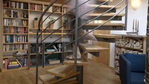 A spiral staircase in a room with wooden bookshelves filled with books, a small table with a plant, and a blue chair. - Ferienhaus Dornstetten (Dornstetten)