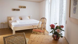 A bedroom with a wooden bed, a chair, a small table, and a vase with flowers. - Ferienhaus Dornstetten (Dornstetten)