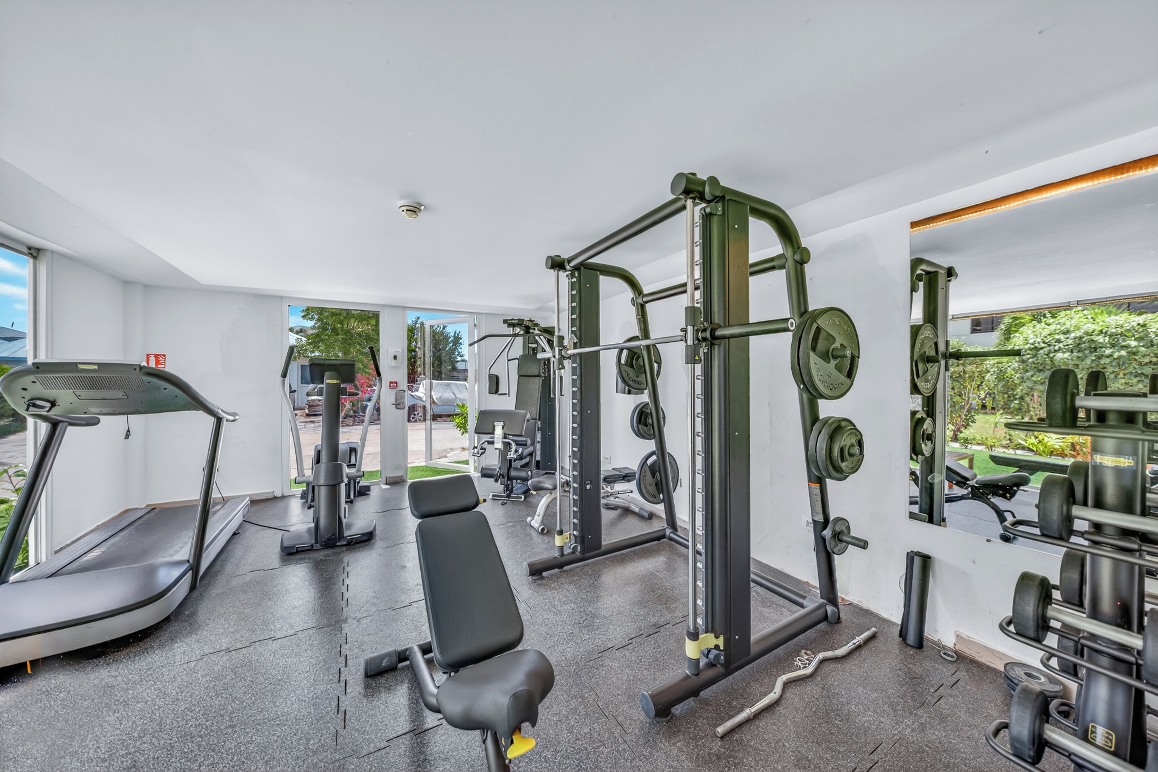 Une salle de sport équipée d’un tapis de course, d’un banc, d’un support à squats et de divers poids.