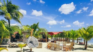 A beach setting with palm trees, a swing chair, and beach chairs. - Hommage Hotel & Residences (Nettle Bay)