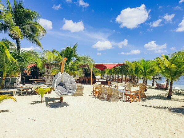 A beach setting with palm trees, a swing chair, and beach chairs. - Hommage Hotel & Residences (Nettle Bay)