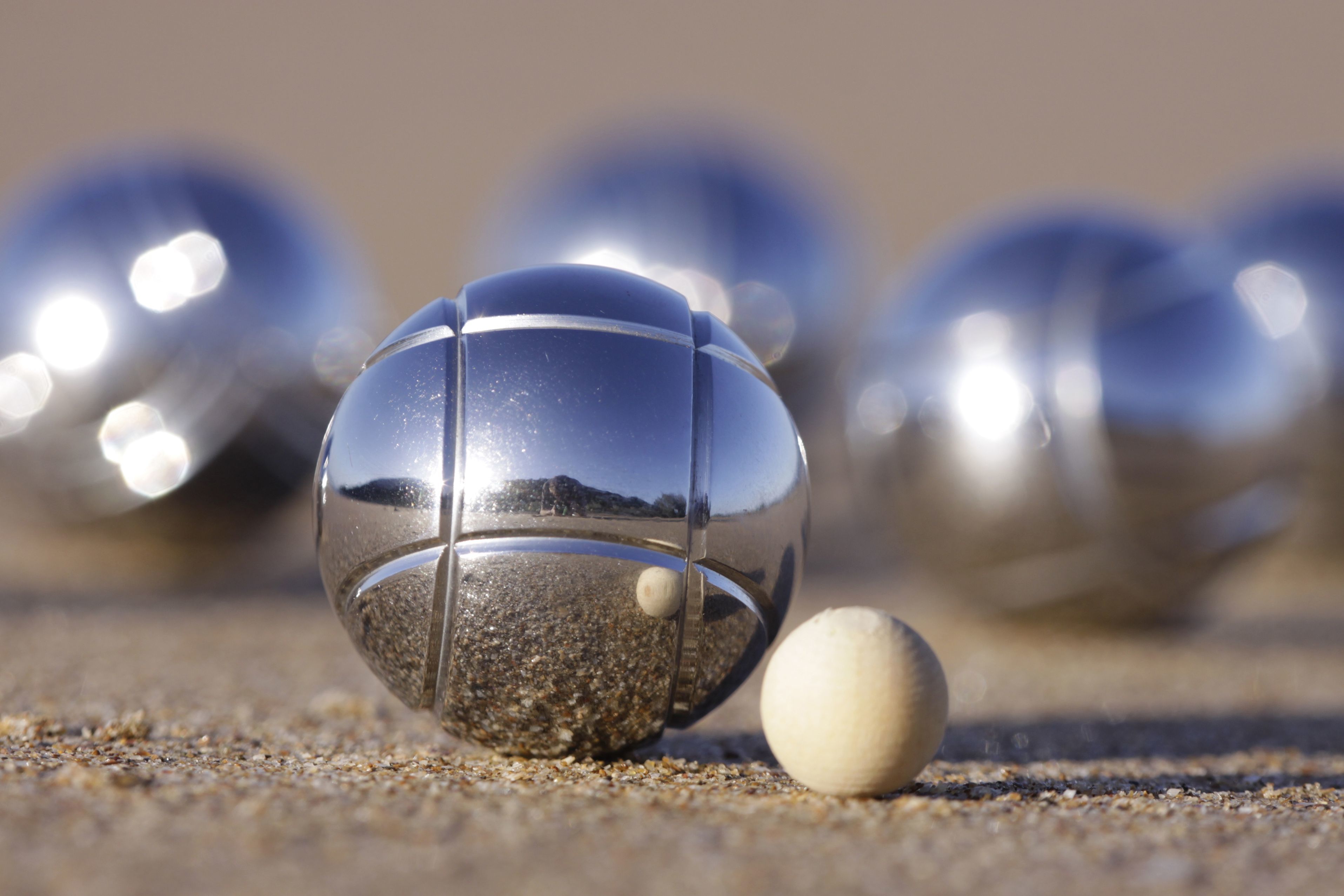 A beach scene with a clear glass ball reflecting the sky and a smaller white ball on the sand.