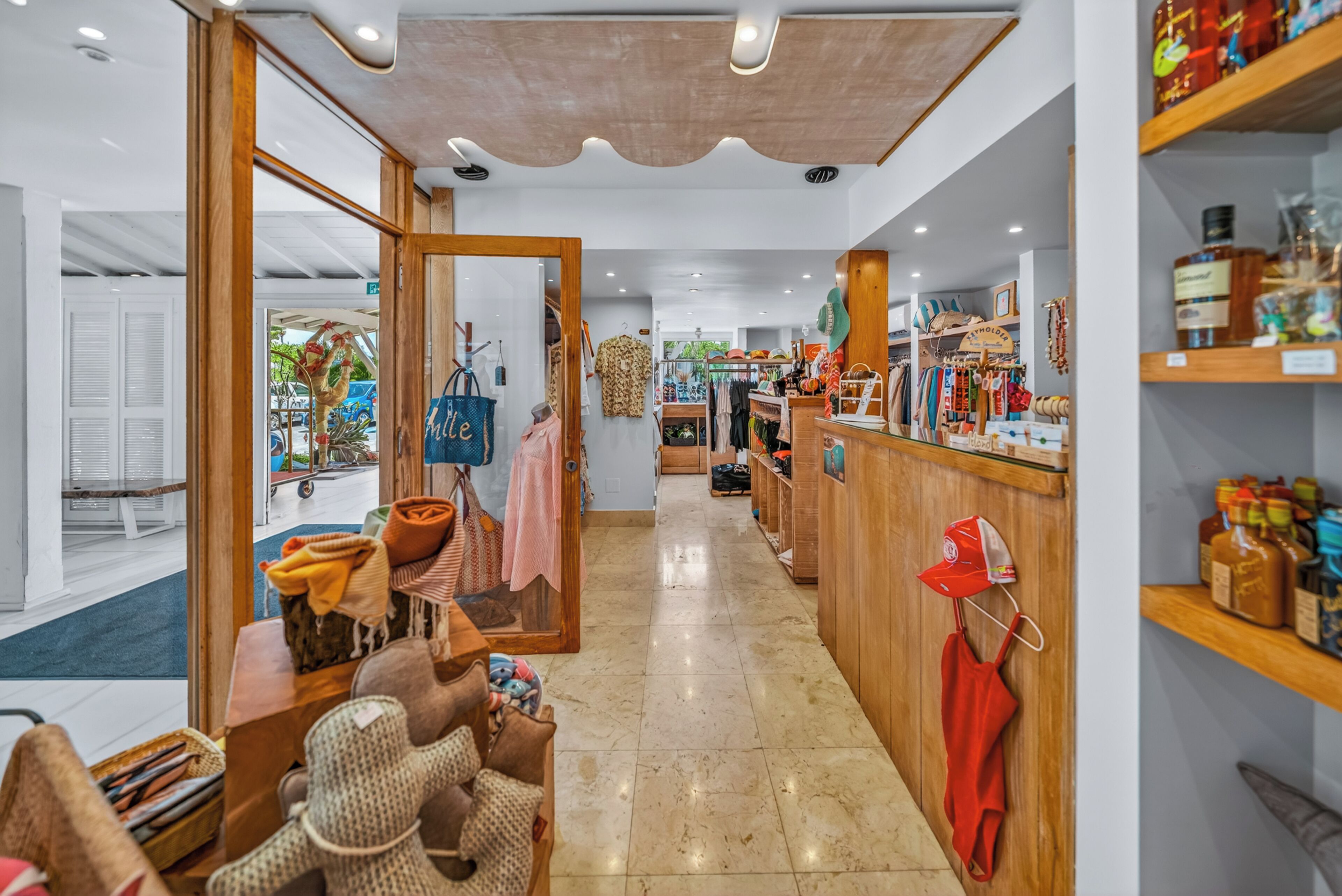 A boutique hotel interior with a central seating area, wooden shelving with various items, and a view of the street outside.