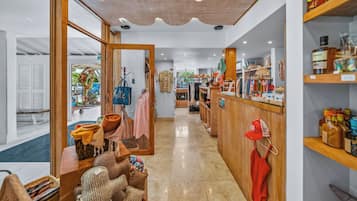 A boutique hotel interior with a central seating area, wooden shelving with various items, and a view of the street outside.