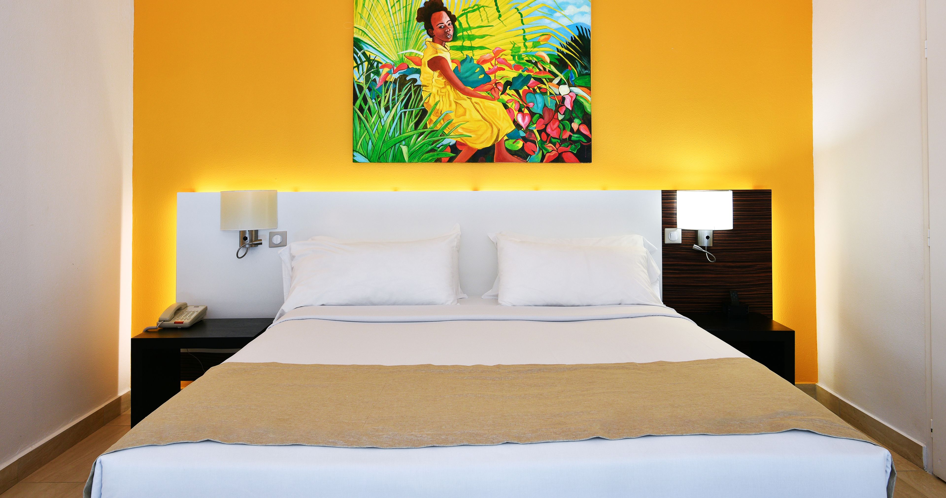 Una habitación de hotel con una cama grande, ropa de cama blanca, una manta color beige, una mesita de noche con un teléfono y un cuadro sobre la cama.