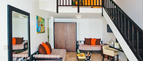 Un salon moderne avec un canapé, une table basse sur laquelle se trouvent des fruits et une bouteille, un bureau avec une chaise et un escalier.
