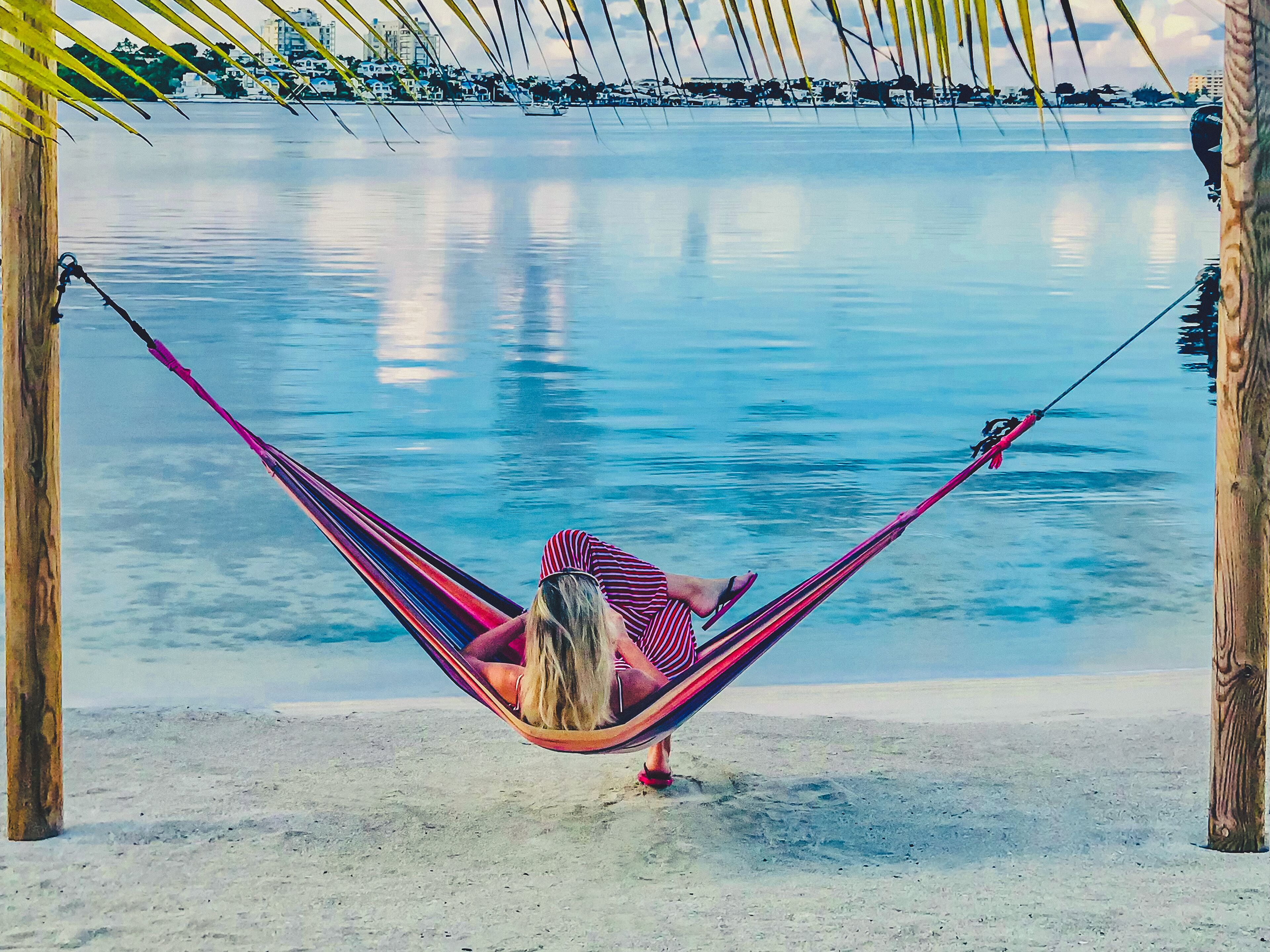 A hammock on a sandy beach with calm water in the background.