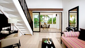 A modern living room with a staircase, a dining area with a view, and a balcony with tropical plants. - Hommage Hotel & Residences (Nettle Bay)