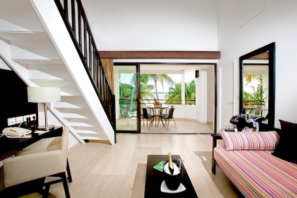 A modern living room with a staircase, a dining area with a view, and a balcony with tropical plants. - Hommage Hotel & Residences (Nettle Bay)