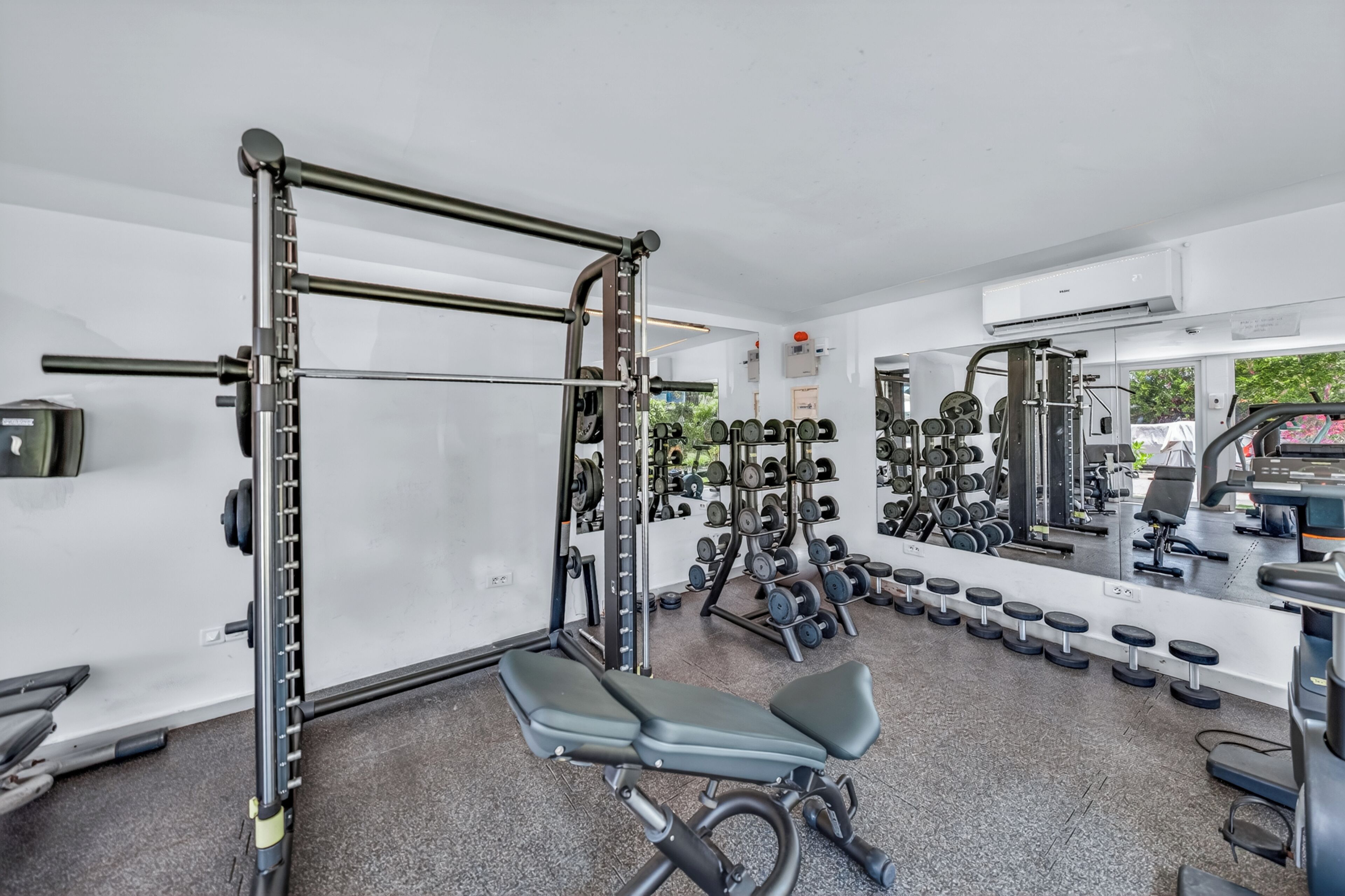 A gym with various exercise equipment, including a squat rack, dumbbells, and a bench.