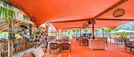 Un área de comedor al aire libre con mesas, sillas, un bar y vista al mar.