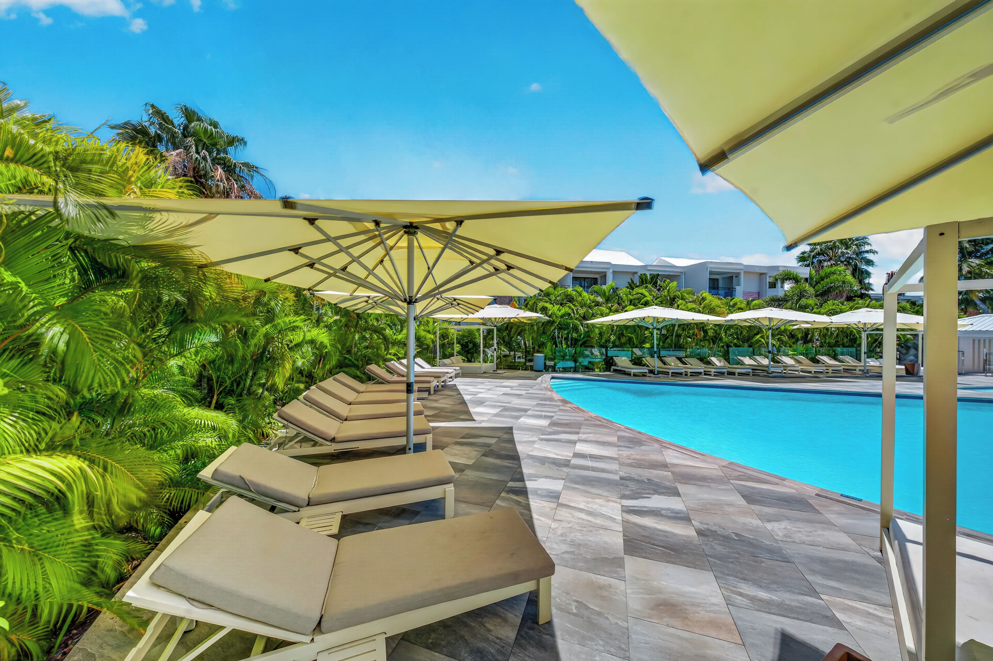 A poolside area with lounge chairs and umbrellas, surrounded by lush greenery.