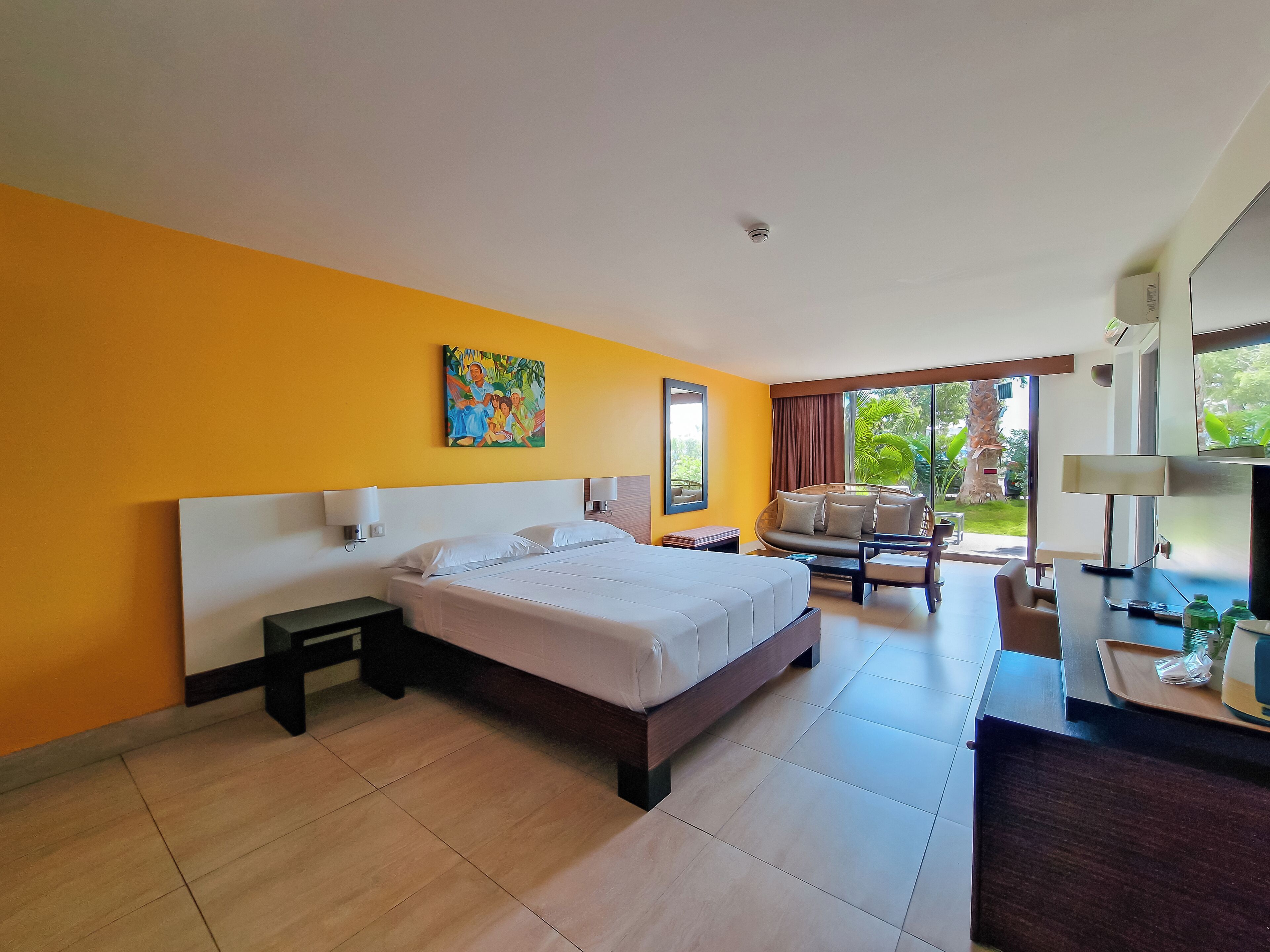 Habitación de hotel con cama, escritorio, silla, televisor y ventana con vista a follaje.