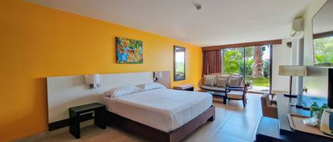 Habitación de hotel con cama, escritorio, silla, televisor y ventana con vista a follaje.