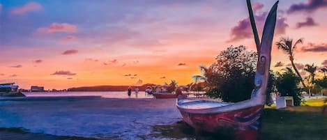 A sunset beach scene with a boat and people walking.