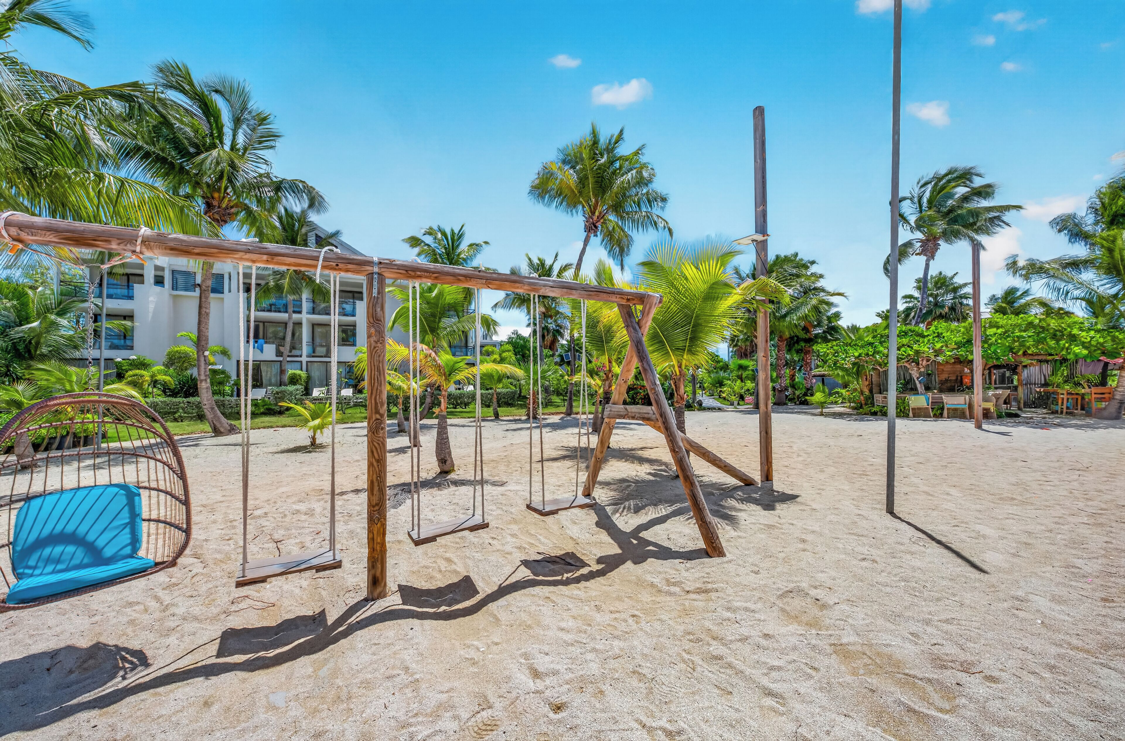 Zona de playa con un columpio, una hamaca y un edificio al fondo.