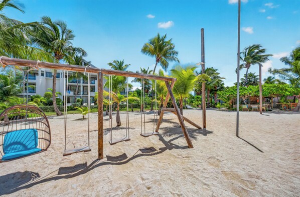 Zona de playa con un columpio, una hamaca y un edificio al fondo.