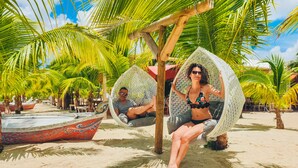 Two people relaxing in wicker swing chairs under palm trees on a sandy beach. - Hommage Hotel & Residences (Nettle Bay)