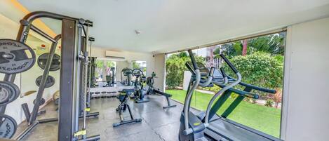 Ett gym med konditionsmaskiner, utrustning för styrketräning och utsikt över en välskött trädgård.