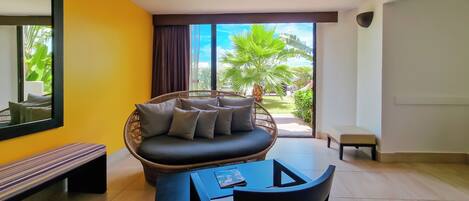 A room with a sofa, a table, and chairs, a bench, and a large window with a view of greenery.
