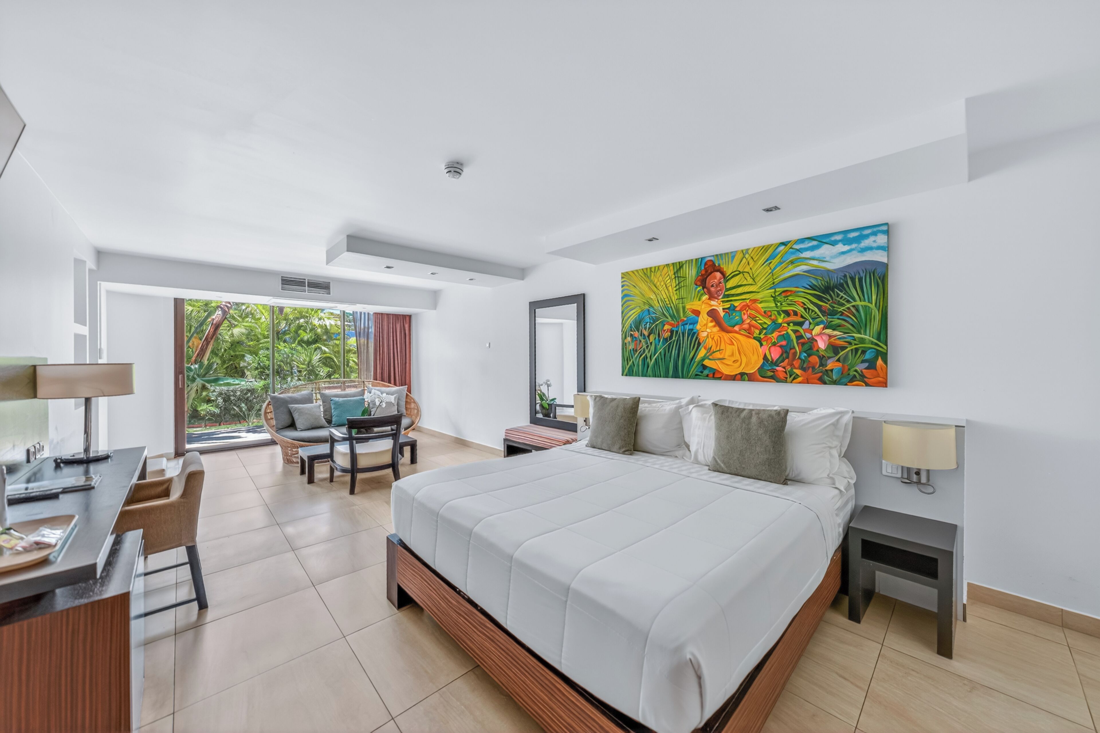 A modern hotel room with a large bed, a desk, and a seating area with a view of the outdoors.