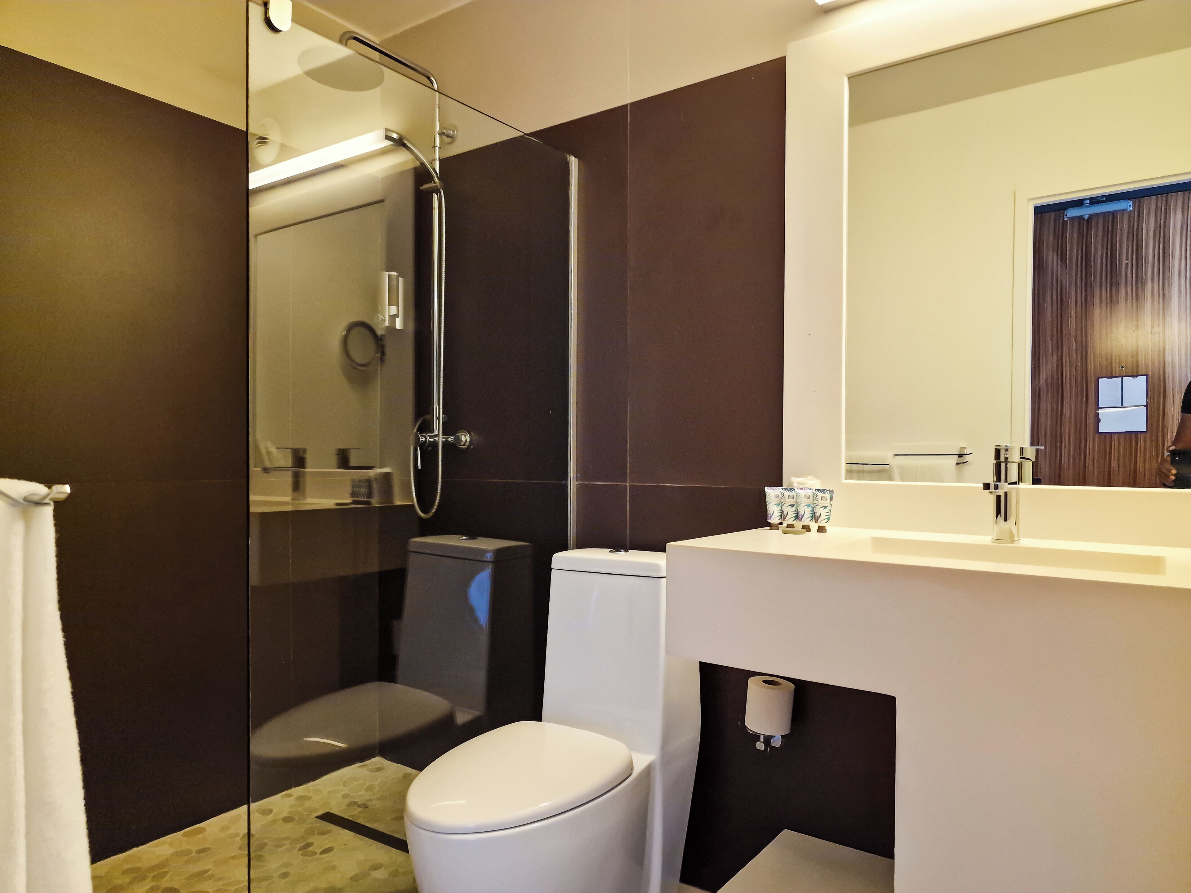 Un baño moderno con ducha de vidrio, inodoro y lavamanos con espejo.