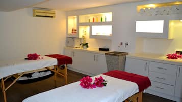 Relax in a serene space with two massage tables, a sink, and shelves.