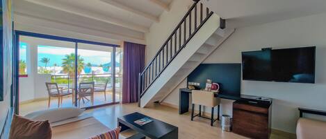 A modern living room with a staircase, a flat-screen TV, and a balcony with a view of the ocean.