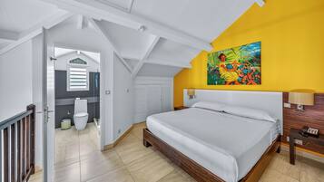 Un dormitorio con una cama, un cuadro, una mesita de noche y un baño visible a través de una puerta abierta.
