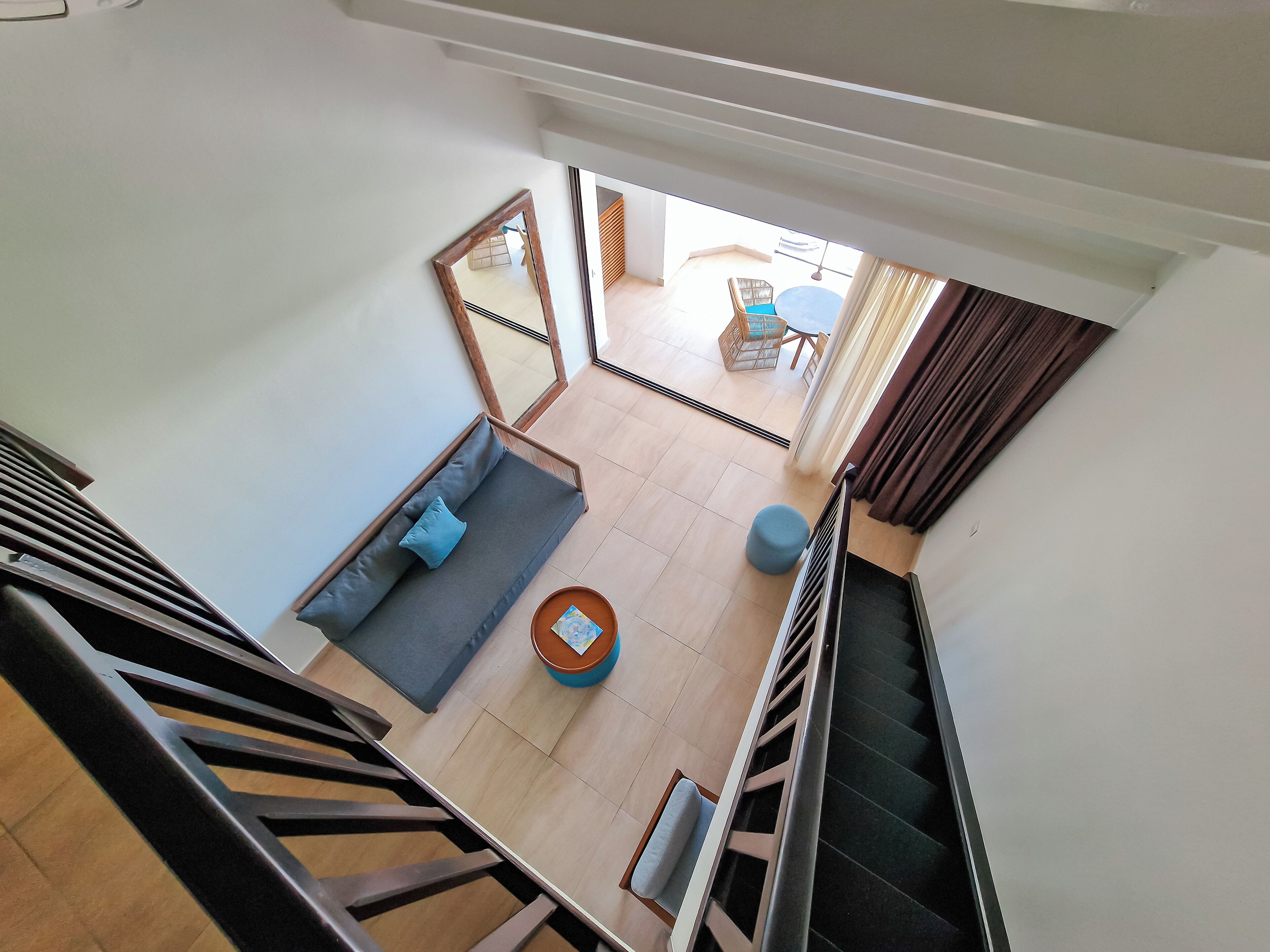 A modern interior with a staircase, a sofa, a round table, and a view of an outdoor area.